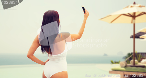 Image of young woman taking selfie with smartphone on beach