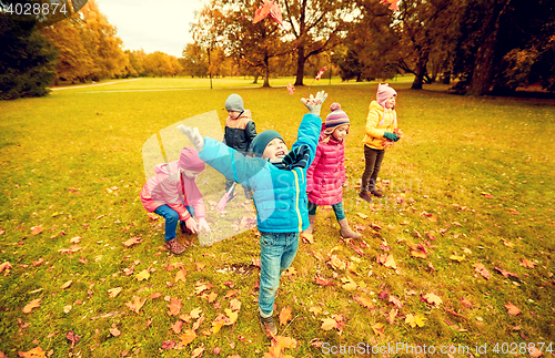 Image of happy children playing with autumn leaves in park