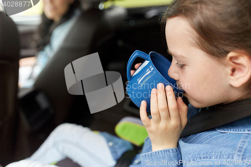 Image of little girl driving in car and drinking from cup