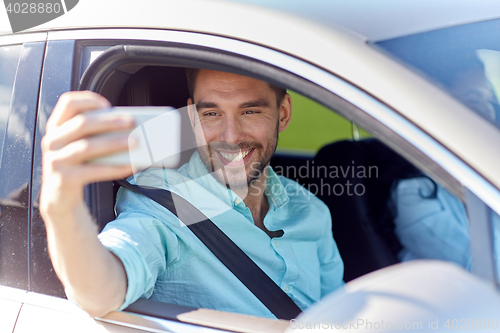 Image of happy smiling man with smartphone driving in car