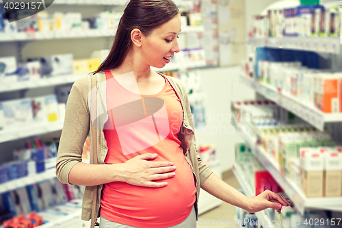 Image of happy pregnant woman choosing medicine at pharmacy