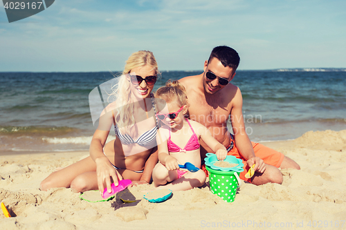 Image of happy family playing with sand toys on beach