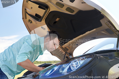 Image of man with open hood of broken car at countryside