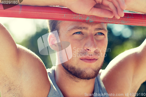 Image of young man exercising on horizontal bar outdoors