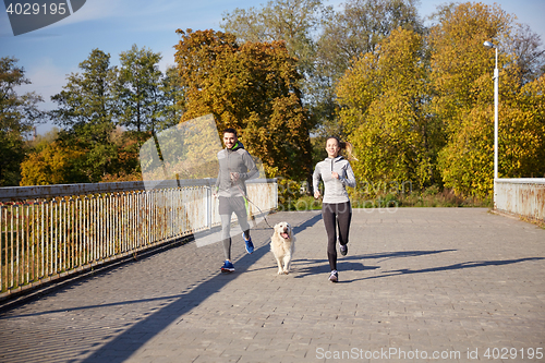 Image of happy couple with dog running outdoors