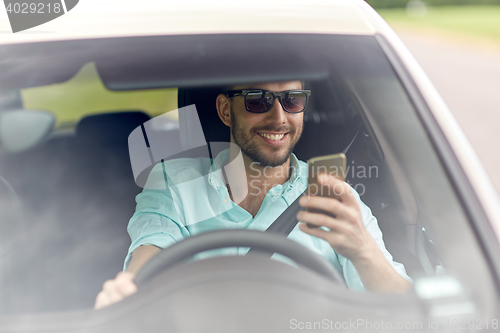 Image of happy man in shades driving car with smartphone