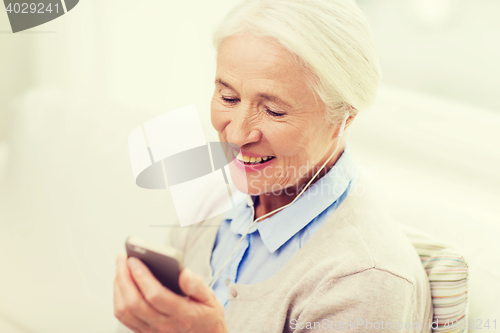 Image of senior woman with smartphone and earphones at home