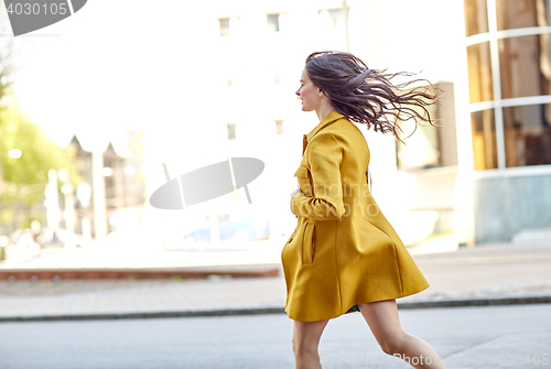 Image of happy young woman running along on city street