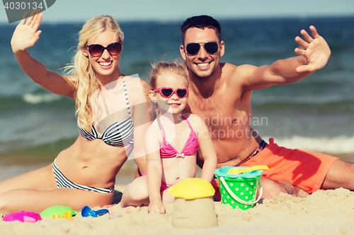 Image of happy family with sand toys waving hands on beach