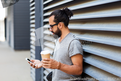 Image of man with coffee texting on smartphone in city