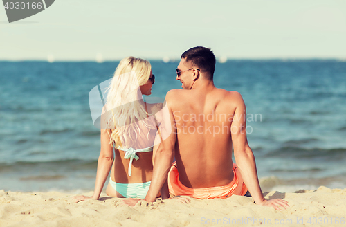 Image of happy couple in swimwear sitting on summer beach