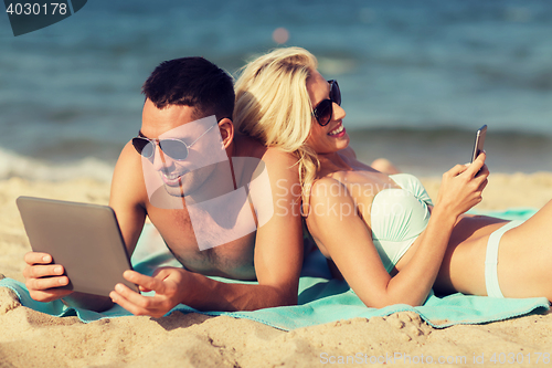 Image of happy couple with tablet pc sunbathing on beach