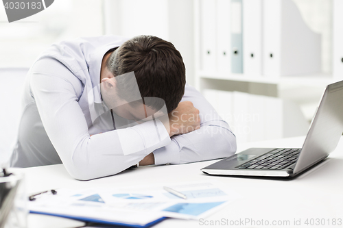 Image of businessman with laptop and papers in office
