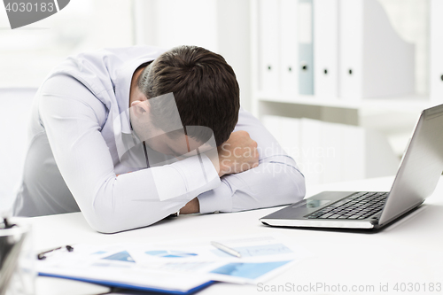 Image of businessman with laptop and papers in office