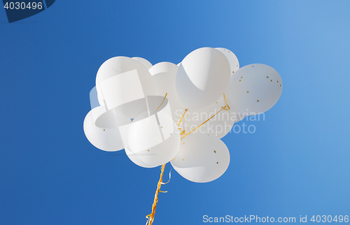 Image of close up of white helium balloons in blue sky