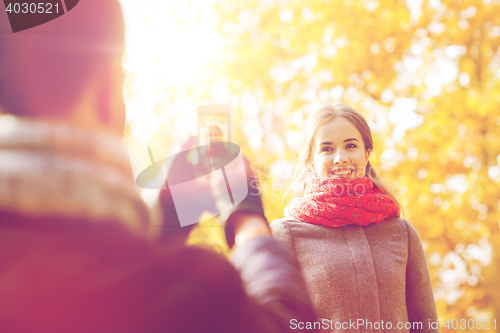 Image of smiling couple with smartphone in autumn park