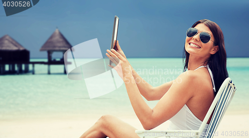 Image of smiling woman with tablet pc sunbathing on beach