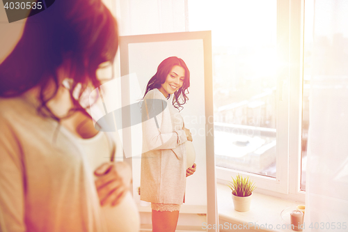 Image of happy pregnant woman looking to mirror at home