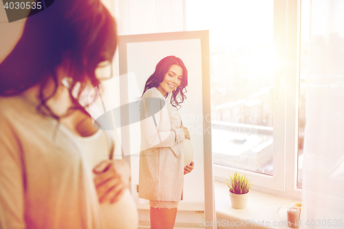 Image of happy pregnant woman looking to mirror at home
