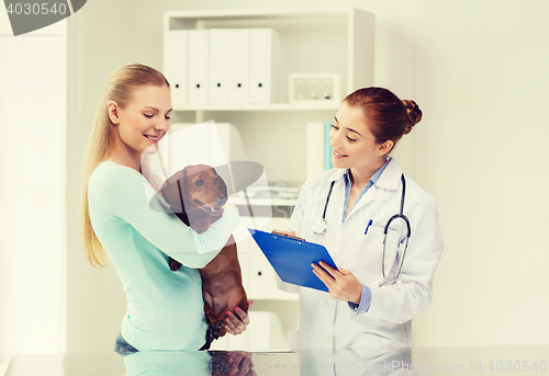 Image of happy woman with dog and doctor at vet clinic