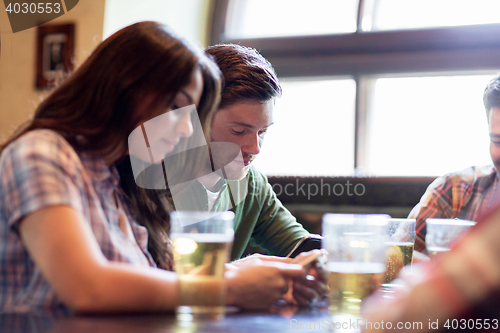 Image of friends with smartphones drinking beer and at pub