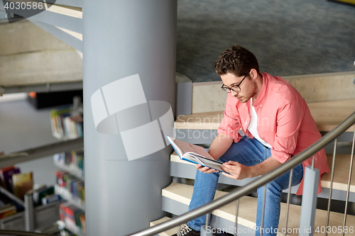 Image of student boy or young man reading book at library