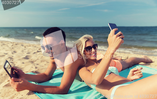 Image of happy couple with modern gadgets lying on beach