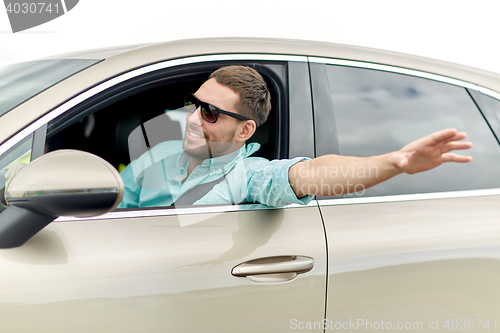 Image of happy man in shades driving car and waving hand