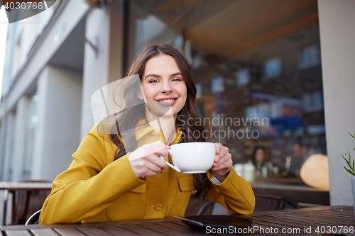 Image of happy woman drinking cocoa at city street cafe