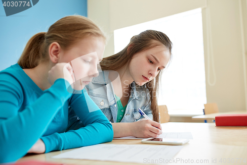 Image of student girls with smartphone writing school test