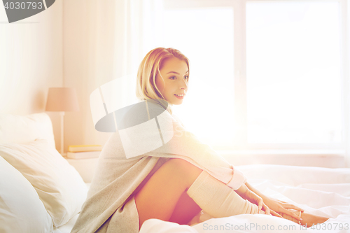 Image of happy young woman sitting in bed at home