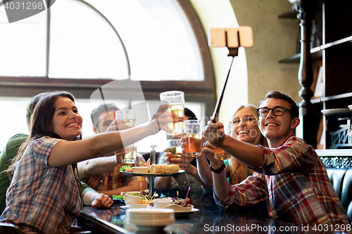 Image of happy friends with selfie stick at bar or pub
