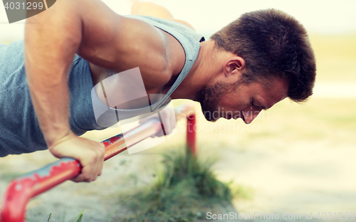 Image of young man exercising on horizontal bar outdoors