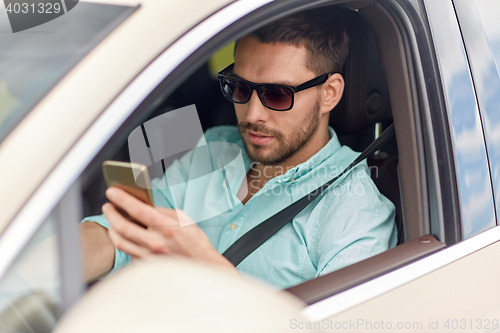 Image of man in sunglasses driving car with smartphone