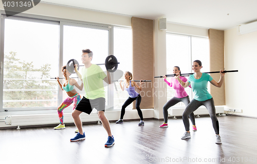 Image of happy people exercising with barbell bars in gym
