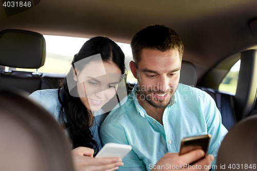 Image of man and woman with smartphones driving in car