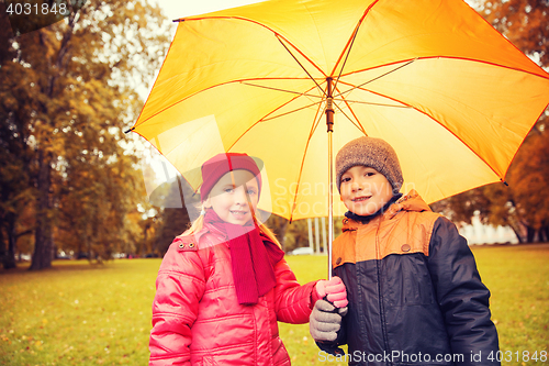 Image of happy boy and girl with umbrella in autumn park