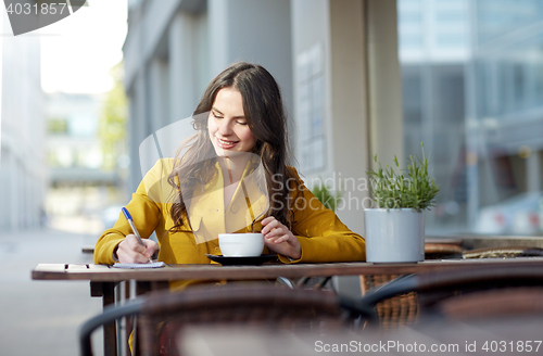 Image of happy woman with notebook drinking cocoa at cafe