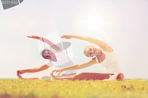 Image of smiling couple making yoga exercises outdoors