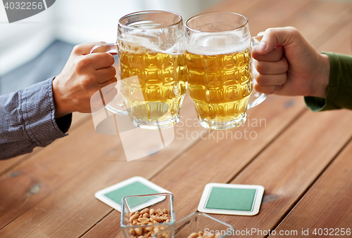 Image of close up of hands clinking beer mugs at bar or pub