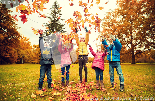 Image of happy children playing with autumn leaves in park