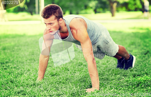 Image of young man doing push ups on grass in summer park