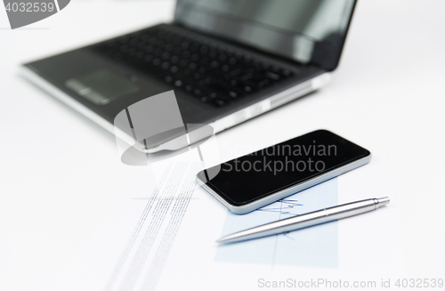 Image of close up of smartphone, laptop and pen on table