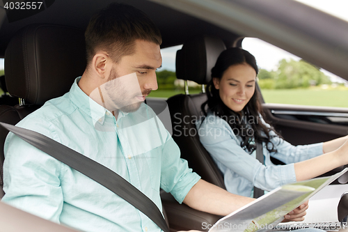 Image of happy man and woman with road map driving in car