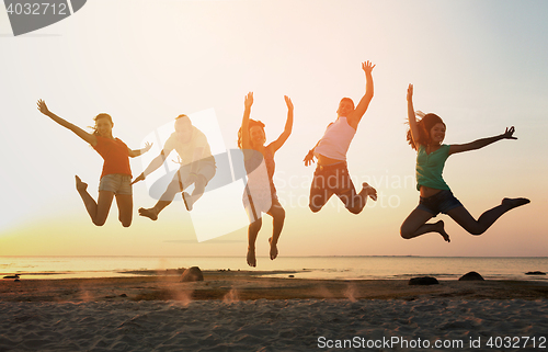 Image of smiling friends dancing and jumping on beach
