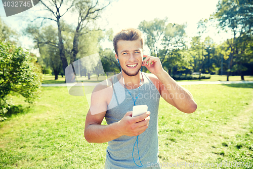 Image of happy man with earphones and smartphone at park