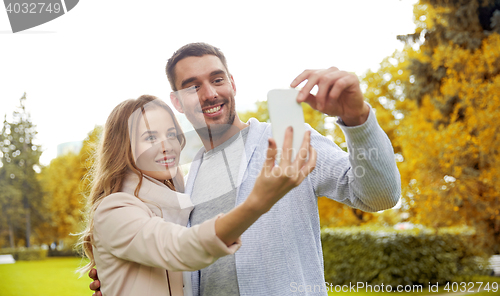 Image of happy couple with smartphone taking selfie in park