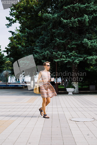 Image of Young brunette woman with coffee cup walking in city