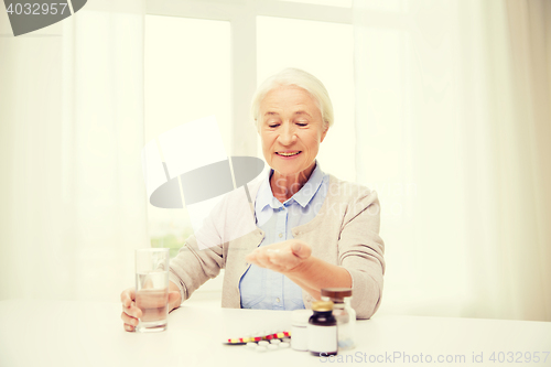 Image of happy senior woman with water and medicine at home