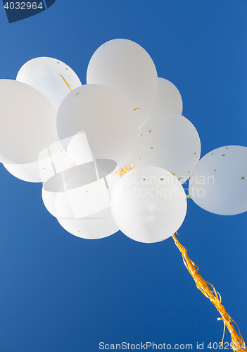 Image of close up of white helium balloons in blue sky